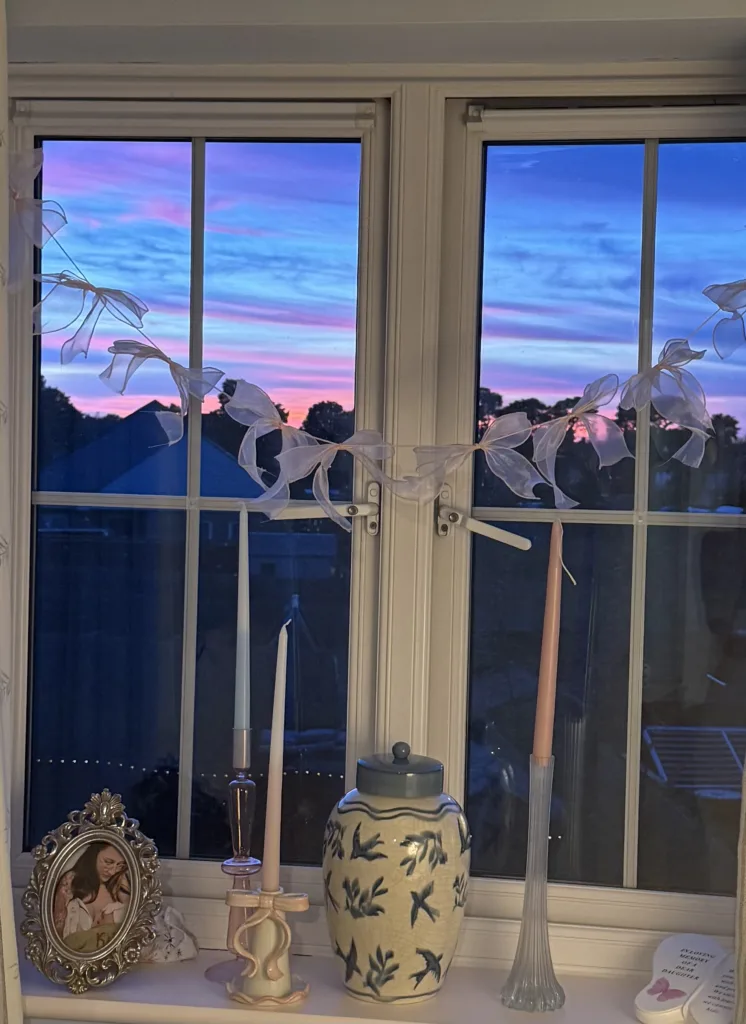 A window with a glorious sunset, on the window sill is a framed photo of Lauren and kitty and Kitty's ashes