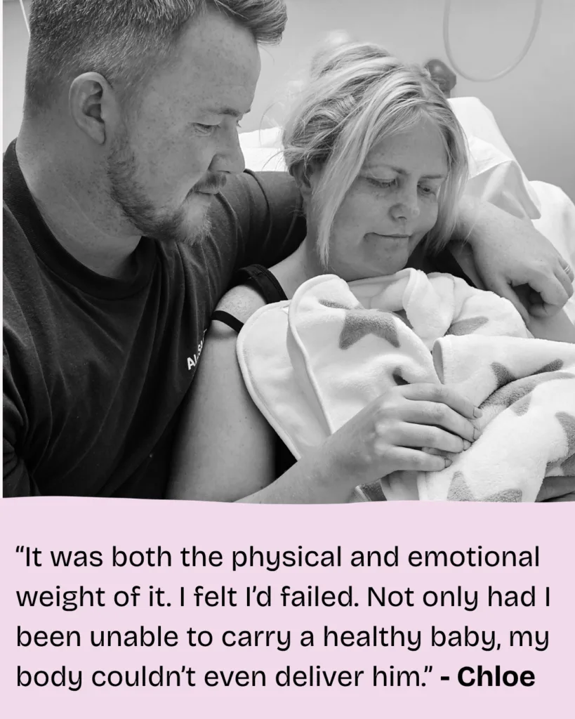 a A black and white photo of Chloe and her partner gazing down at their baby boy, Ronnie, who is wrapped in a blanket and in Chloe's arms.